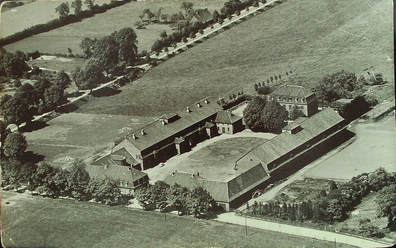 Historische Luftaufnahme des Gut Stellmoor in Schwarzweiß: die langen Stallgebäude und das Herrenhaus, ringsum Felder, Wege und Baumreihen